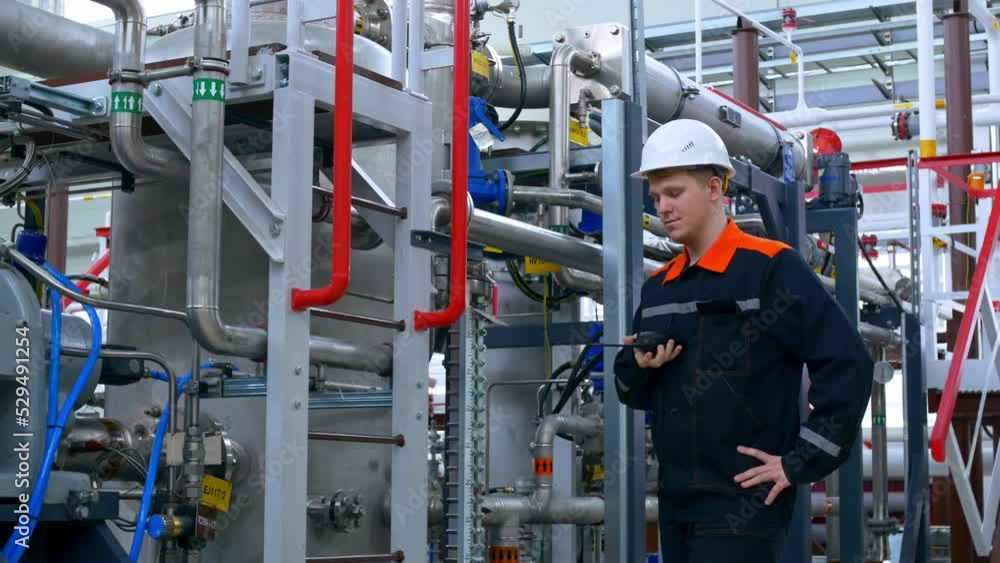 An engineer in a white helmet and overalls checks the operation of compressor equipment at the plant. An engineer inspects industrial equipment. Working at a gas liquefaction plant. An engineer in a white helmet and overalls checks the operation of compressor equipment at the plant. An engineer inspects industrial equipment. Working at a gas liquefaction plant.