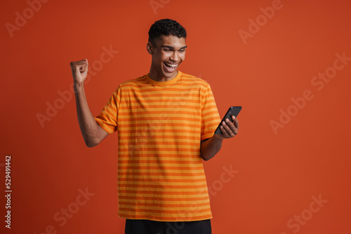 Young handsome enthusiastic african man with raised hand holding phone