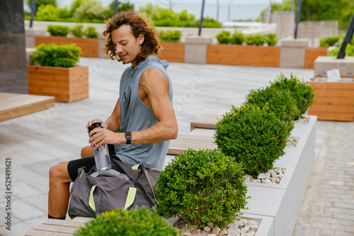 Portrait of young long-haired athletic man opening bottle of water photo