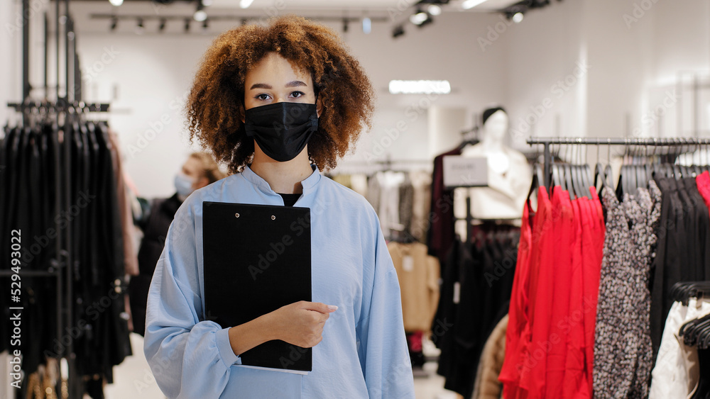 Black Friday. African american welcoming woman saleswoman girl consultant in medical mask boutique store worker standing in shopping mall inviting to buy clothes discounts sale low prices invitation Black Friday. African american welcoming woman saleswoman girl consultant in medical mask boutique store worker standing in shopping mall inviting to buy clothes discounts sale low prices invitation