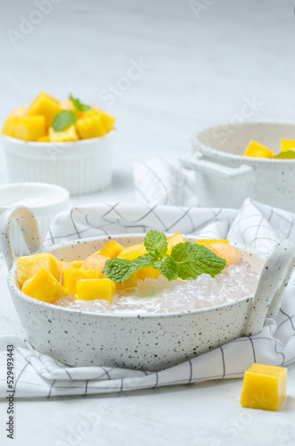 The thai dessert food modern style : The homemade sago in coconut milk with topping is mango cut into squares and cantaloupe ball in the white bowl and placed on tablecloth plaid on the marble table.