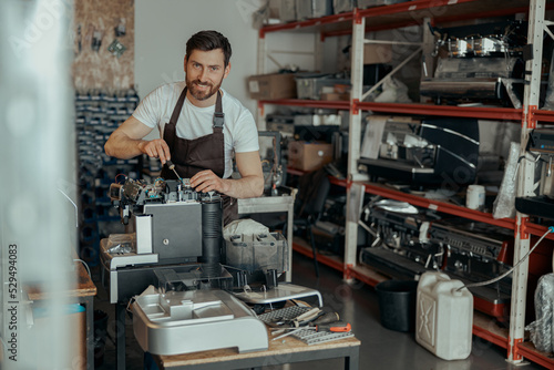 Man worker in uniform checking coffee machine in own workshop and looking camera
