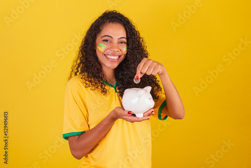 Young black Brazilian woman, soccer fan. holding piggy bank and coin. finance, economy, retirement. photo