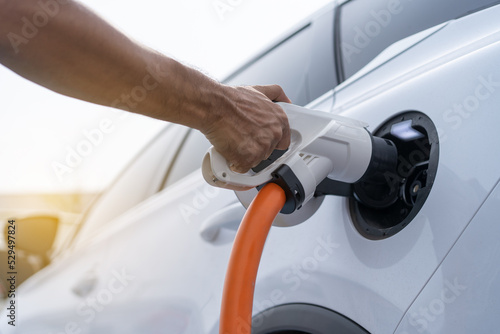 The male plugs the power cable in the electric car to charge.