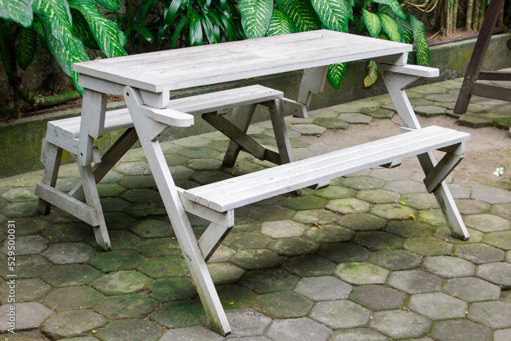 empty wooden white benches with a chair on the grass in the garden empty wooden white benches with a chair on the grass in the garden