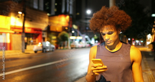 African black man looking at cellphone device while walking at night in downtown city