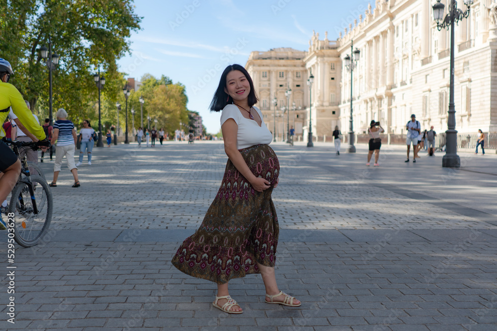 young happy and beautiful Asian Korean woman posing outdoors happy and cheerful pregnant showing her belly proud smiling in pregnancy and maternity concept
