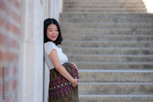 young happy and beautiful Asian Korean woman posing outdoors happy and cheerful pregnant showing her belly proud smiling in pregnancy and maternity concept