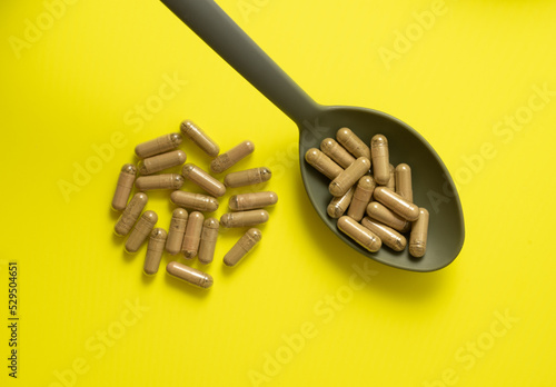 kratom pills composition on yellow background with spoon, handful of kratom pills