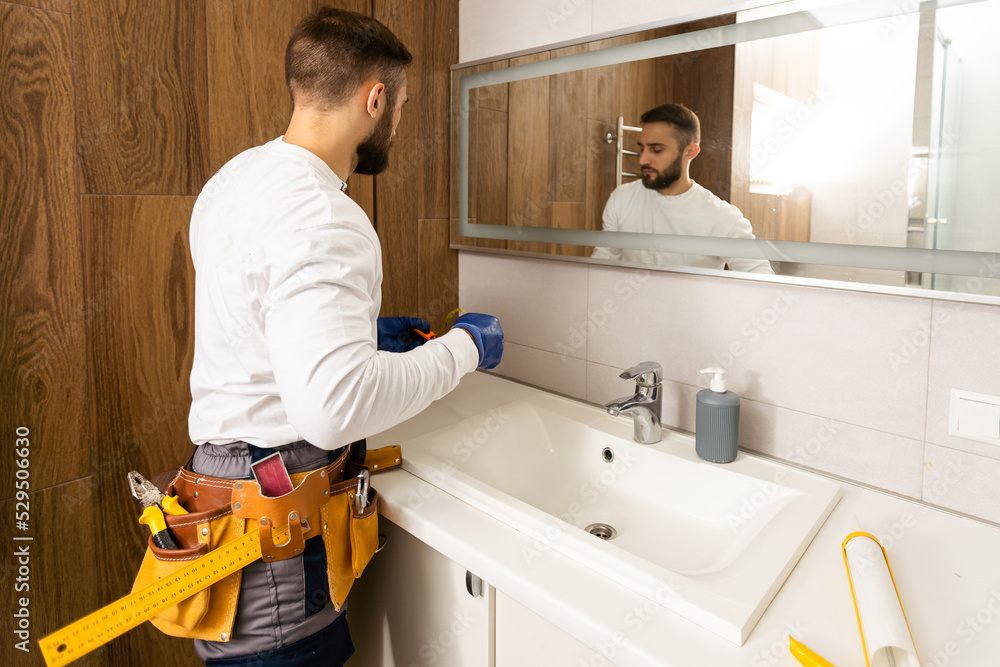 Fototapeta premium Man installing a mirror on wall in his renewed bathroom