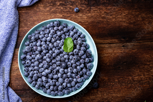 Fresh blueberries berries in a plate on a dark wooden background.