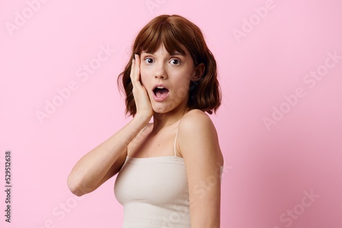 a happy, very emotional woman stands on a pink background with her mouth wide open in surprise and holds her hand near her face