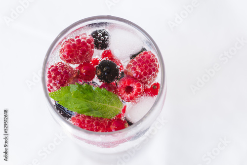 Carbonated drinks with fresh berries and ice. Fresh cold sparkling bubble water with mint, raspberry, black and red currant in transparent glass with ice, top view macro. Food and drink concept
