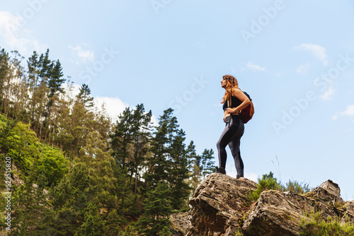 caucasian hiker woman standing on a rock while contemplating the forest and mountain landscape while hiking. weekend outdoor activities