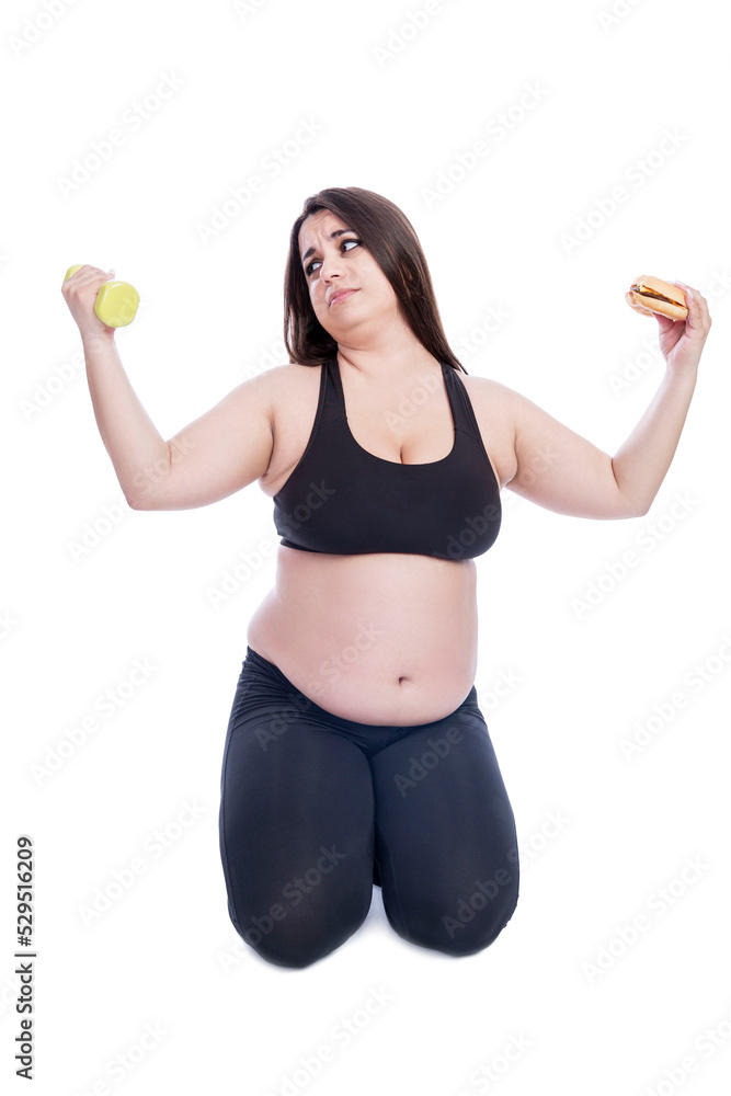 Overweight woman in black sportswear with dumbbells and a hamburger in her hands. Sports and diet in the fight against obesity. Isolated on white background. Vertical. Overweight woman in black sportswear with dumbbells and a hamburger in her hands. Sports and diet in the fight against obesity. Isolated on white background. Vertical.