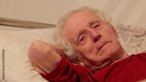 Senior man eighty nine years old lying in bed, yawning, rubbing eyes and nose and sneezing
