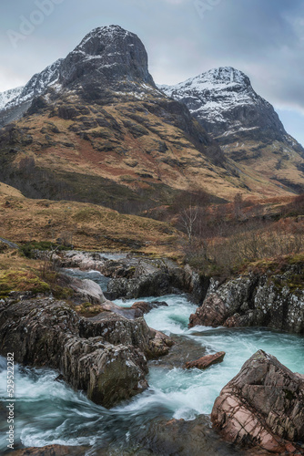 Epic landscape image of vibrant River Coe flowing beneath snowcapped mountains in Scottish Highlands