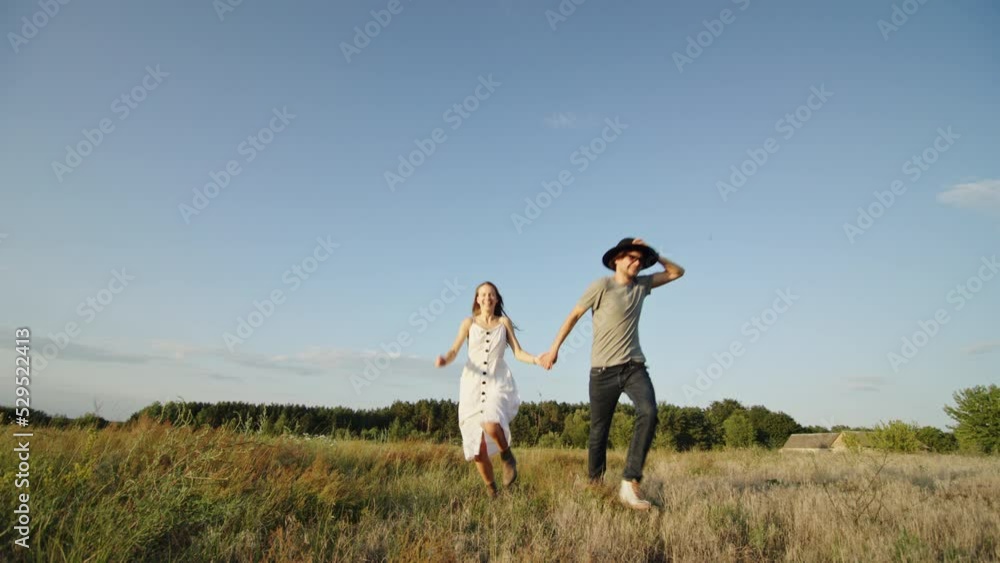 Romantic stylish couple holding hands and running on grassy field in countryside Romantic stylish couple holding hands and running on grassy field in countryside