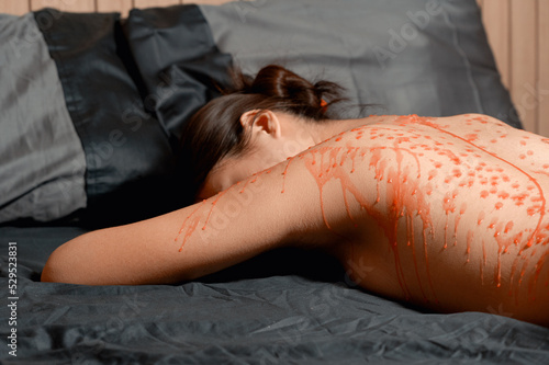 Red wax on skin of young submissive woman on a bed