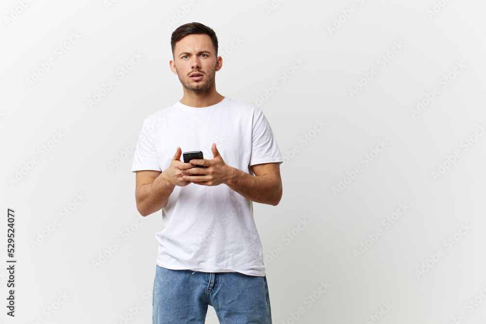 Confused unhappy tanned handsome man in basic t-shirt get shock info from phone message posing isolated on over white studio background. Copy space Banner Mockup. Distance online communication concept Confused unhappy tanned handsome man in basic t-shirt get shock info from phone message posing isolated on over white studio background. Copy space Banner Mockup. Distance online communication concept