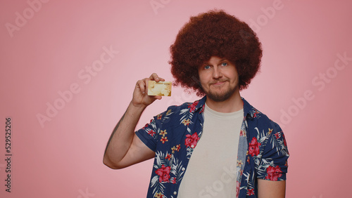 Happy tourist man showing plastic credit bank card advertising transferring money cashless, purchases online shopping, sale discount, internet order delivery purchase. Young guy boy on pink background