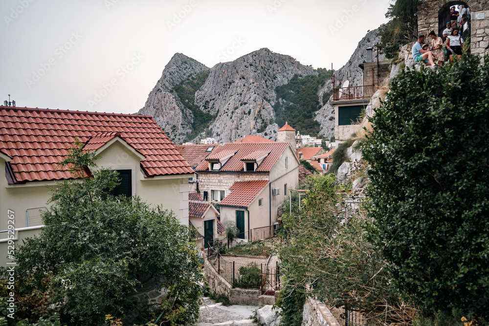 Tourists climbing stone stairs of medieval town of Omis, located under mighty, dangerous and steep rocky cliffs used for pirates to hide