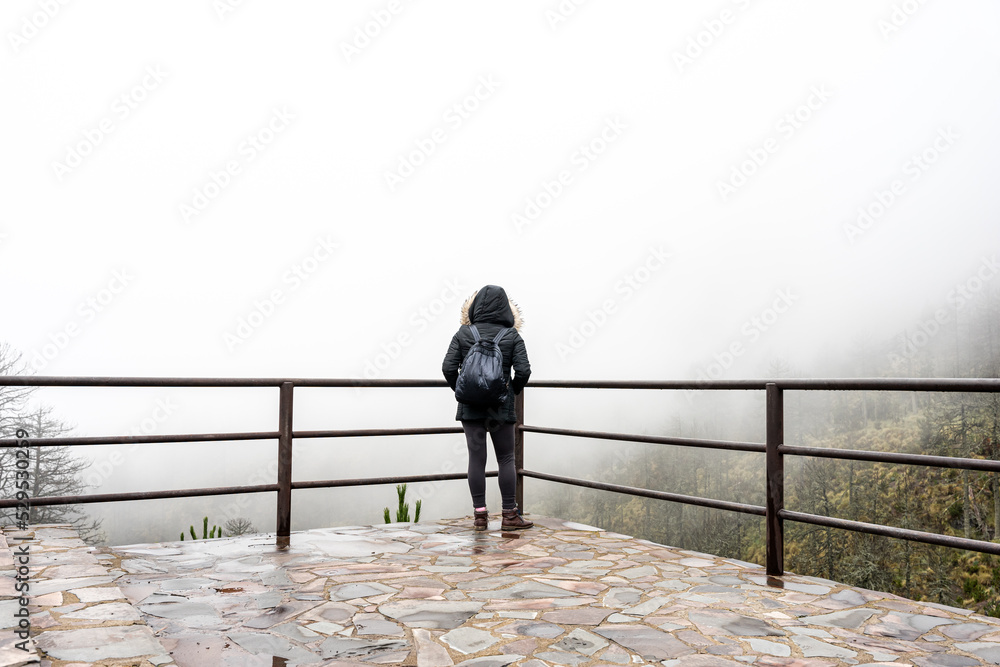 Tourist woman in Black coat is looking at the misty forest. Wanderlust travel concept, space for text, atmospheric epic moment, Nevado de Colima.