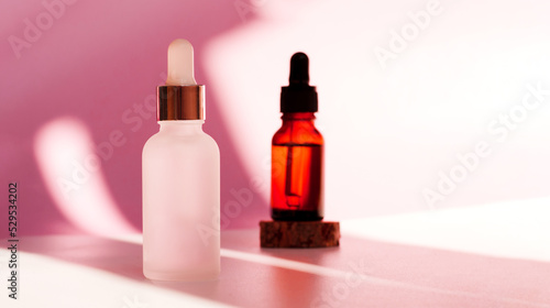 Banner of two transparent amber and frozen glass dropper bottles on pink background in the sunlight. Wooden podium. Pipette with fluid hyaluronic acid, serum, retinol. Cosmetics, healthcare, beauty 