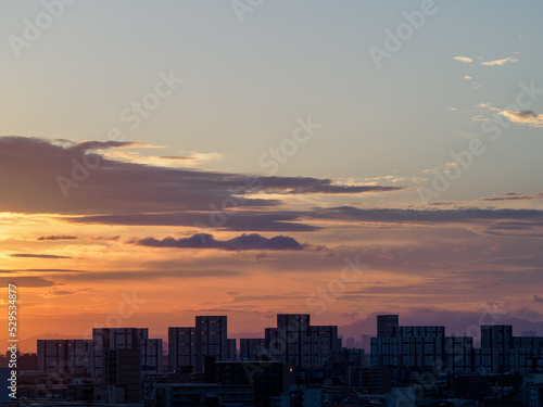 都市の夜明け。日の出とともに空と雲がオレンジ色に染まり、ビル群はシルエットとして写す