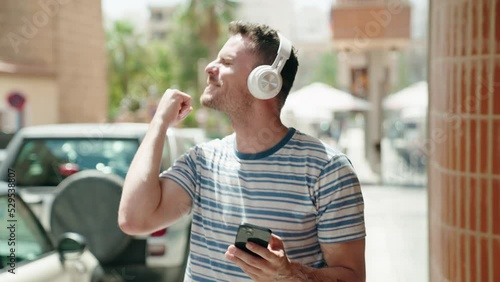 Young hispanic man listening to music and dancing at street
