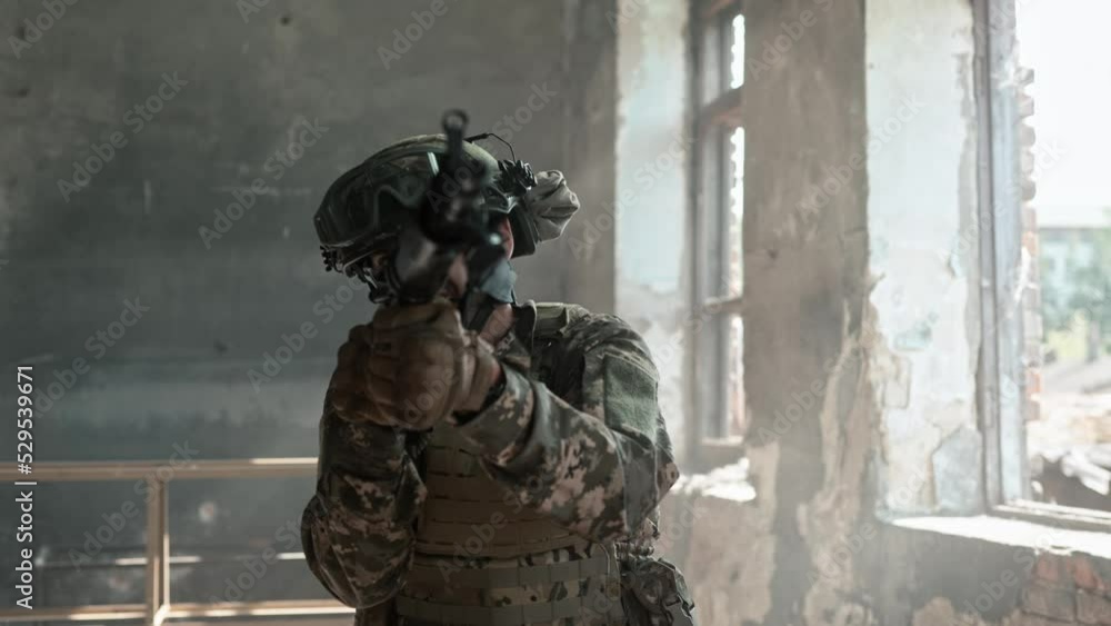 Young male soldier in helmet and army clothing moves along the dark ruined room with window with gun rifle. Close up of military man in war in Ukraine. Soldier with rifle watch and cover the back Young male soldier in helmet and army clothing moves along the dark ruined room with window with gun rifle. Close up of military man in war in Ukraine. Soldier with rifle watch and cover the back