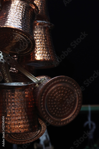Bunch of Turkish embossed cooper bronze coffee pots hanging in the oriental market place in Heildeberg. Closep, side view. Black Background. Copy Space
