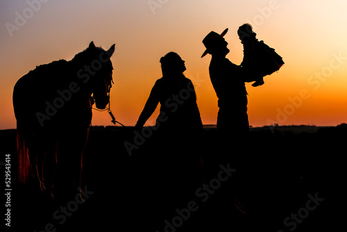 silhouette of farm family, woman holding horse and gaucho father holding daughter