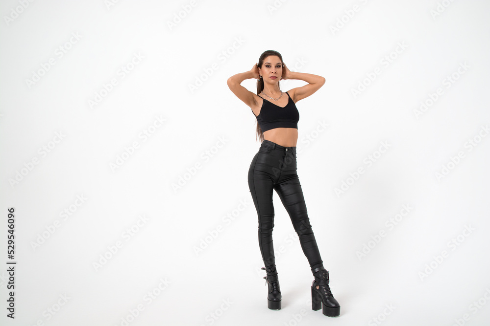 a brunette girl with long hair in black leather pants and boots poses on a white background.youth fashion.