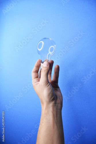 Man's hand holding bulb on blue background.
