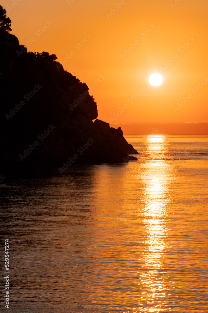 Beautiful view of orange sunset with rocks in Calabria, Mediterranean Sea, Italy. Tropical colorful sunrise landscape. Seascape