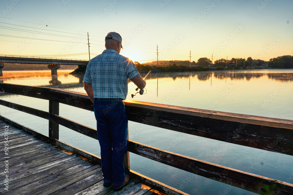 Man fishing off pier with a beautiful sunrise on Tims Ford Lake in Tennessee