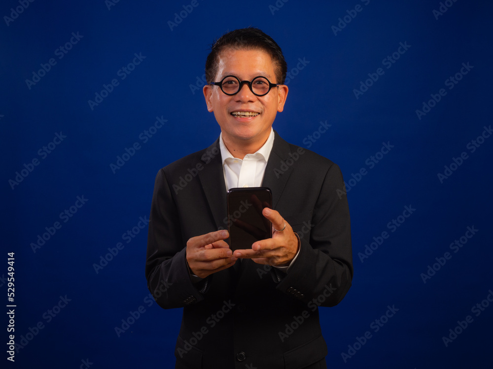 Portrait of smart middle-aged asian confident successful businessman wearing suit holding smartphone isolated on blue background in studio, looking attractive and positive professional leadership Portrait of smart middle-aged asian confident successful businessman wearing suit holding smartphone isolated on blue background in studio, looking attractive and positive professional leadership