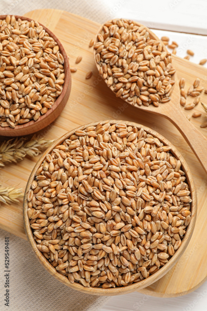 Wheat grains in bowls and spoon on wooden board, flat lay Wheat grains in bowls and spoon on wooden board, flat lay