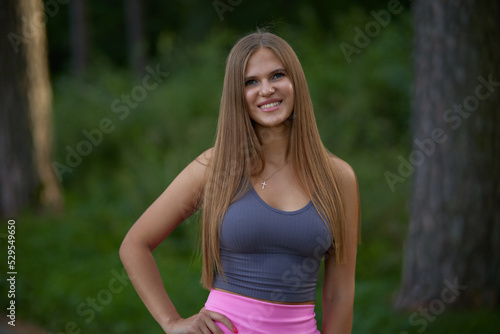 Lovely young woman with sexy boobs in trendy gray top in pink fashionable sports shorts walking on street. Pretty beauty girl fashion model walks in park. Healthy lifestyle. 