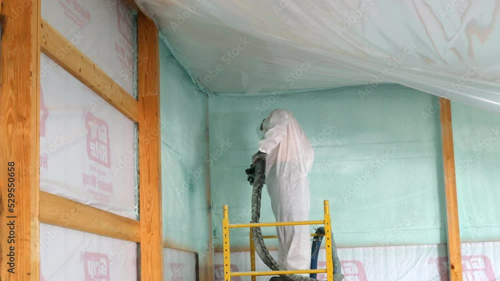 Worker in respirator and Tyvek suit sprays closed cell foam insulation