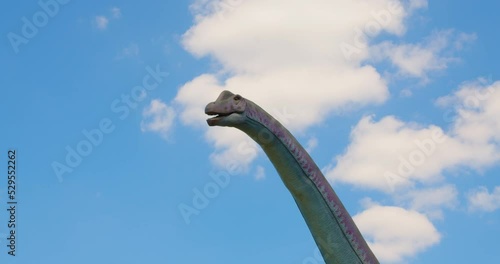 Park attraction place. A dinosaur head in the move. The figure of Stone age monster in close-up on the blue sky background. Vacation, holiday leisure. photo