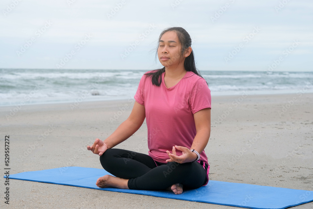 Asian woman practicing yoga at seashore. Beautiful woman meditating around the sea beach at sunrise for health. relaxing in nature