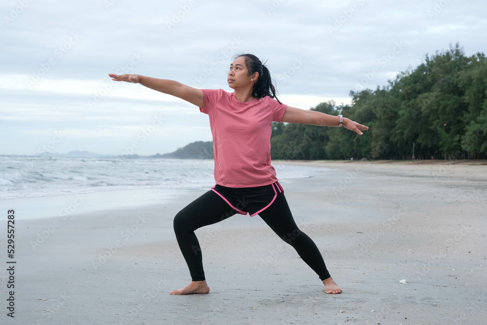 Asian woman practicing yoga at seashore. Young beautiful woman stretching and doing yoga outdoors on blue yoga mat on beach. relaxing in nature Asian woman practicing yoga at seashore. Young beautiful woman stretching and doing yoga outdoors on blue yoga mat on beach. relaxing in nature