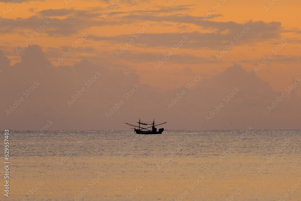 Silhouette of a fishing boat sailing on the ocean water at sunset with golden light reflected on the water surface and soft waves. Summer vacation and travel concept.