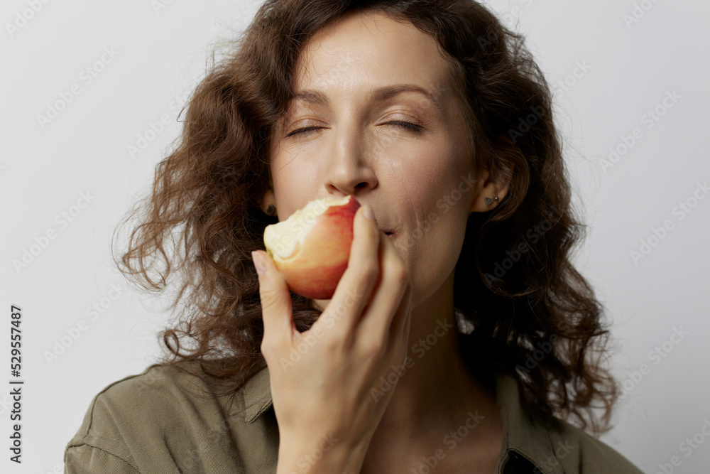 Joyful happy curly beautiful woman in casual khaki green shirt eat apple enjoy fresh juicy fruit posing isolated on over white background. Natural Eco-friendly products concept. Copy space Joyful happy curly beautiful woman in casual khaki green shirt eat apple enjoy fresh juicy fruit posing isolated on over white background. Natural Eco-friendly products concept. Copy space