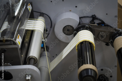 A machine for the production of white self-adhesive labels. The shafts of the machine for winding rolls of tape with a label. Die-cutting and cutting of paper for label production. Selective focus