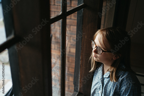 Melancholic primary aged girl in a school uniform looks out a window photo