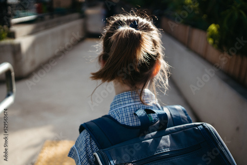 Girl with a ponytail in a school dress with a backpack walks along a path photo