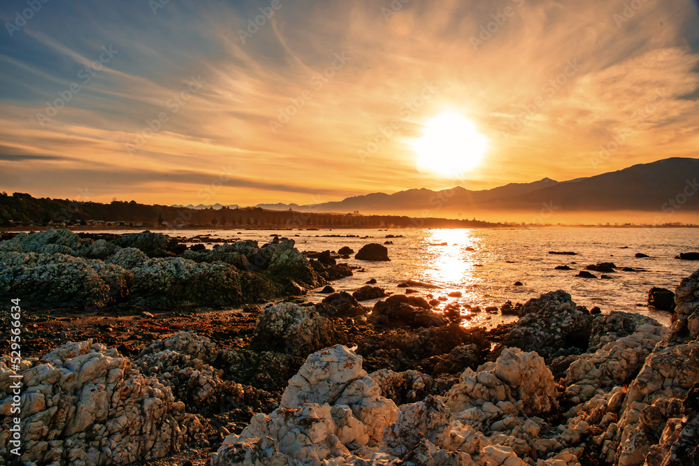 Dramatic orange  cloudscape  sunset at  dusk over the rocks and bay at Kaikoura harbour